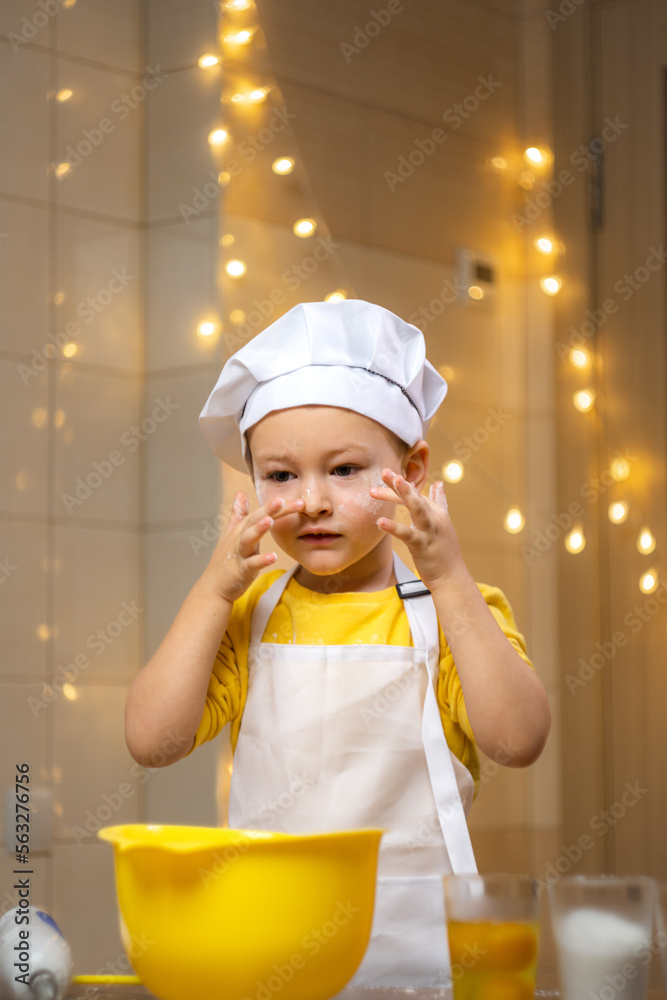 Toddler boy playing with the dough in the kitchen dressed as a chef. Child baking a cake Toddler boy playing with the dough in the kitchen dressed as a chef. Child baking a cake