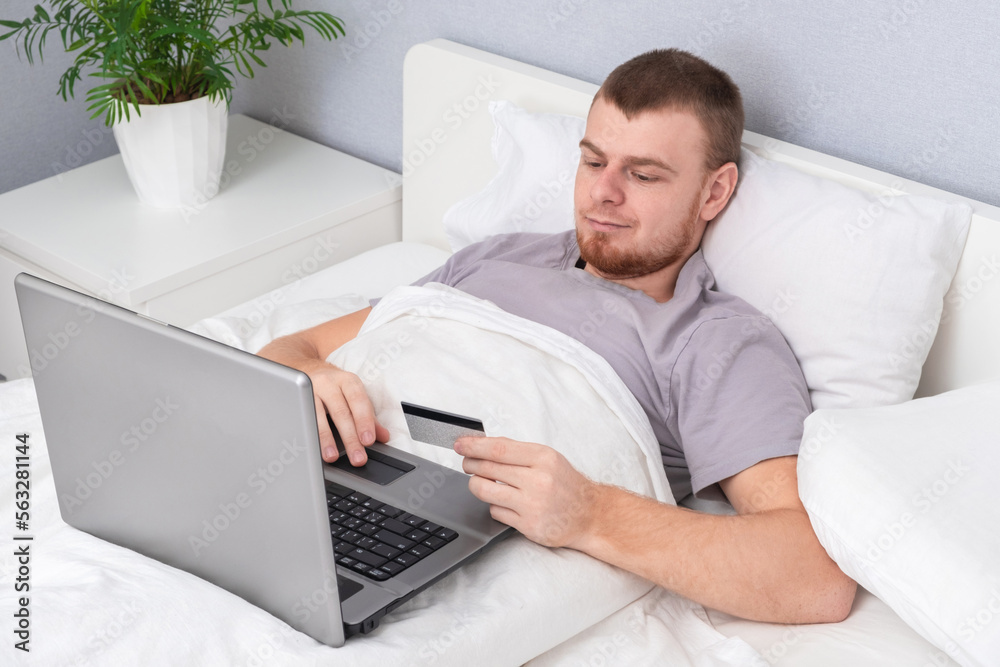 Man with laptop lying in bed. Online shopping without leaving home. Internet surfing. Gambling addiction. Cybersecurity. Black Friday sale. Cyber Monday. Online gift buy. Booking tickets hotels planes Man with laptop lying in bed. Online shopping without leaving home. Internet surfing. Gambling addiction. Cybersecurity. Black Friday sale. Cyber Monday. Online gift buy. Booking tickets hotels planes