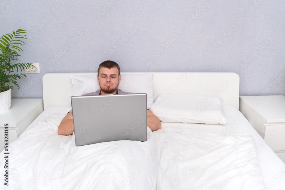 Man with laptop lying in bed. Freelancer works remotely from home. Distance education. Online shopping without leaving home. Internet surfing. Gambling addiction. Black Friday sale. Cyber Monday. Man with laptop lying in bed. Freelancer works remotely from home. Distance education. Online shopping without leaving home. Internet surfing. Gambling addiction. Black Friday sale. Cyber Monday.