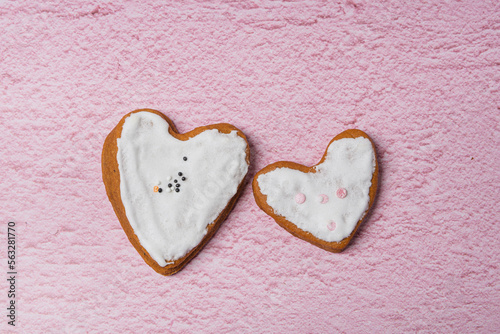 Two handmade gingerbread cookies with white icing in the form of hearts are laid out on a pink background. Flat lay