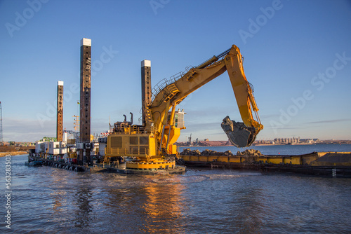 In the port, a large floating dredging excavator scoops up soil from the bottom