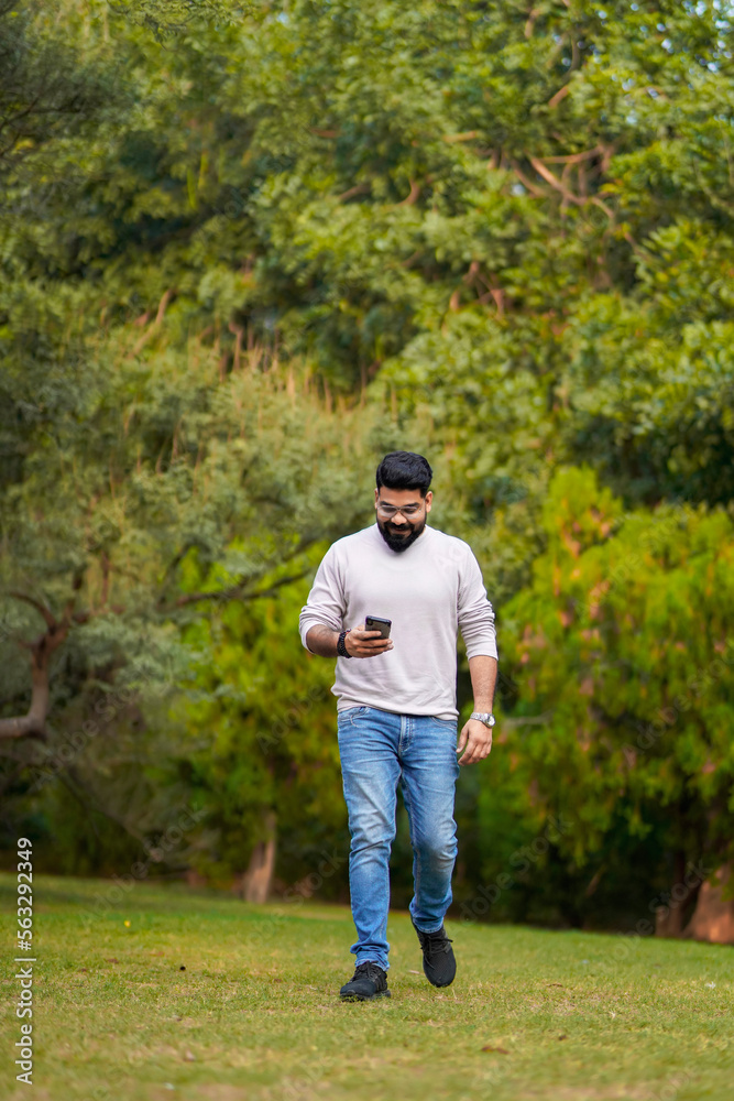 Young indian man using smartphone at park.