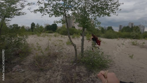 POV cinematic shot  maniac chasing victim in a wasteland outside the city. Tall man in black clothes with rope in hands running after girl in red jacket, sneakers and long hair. True crime concept 