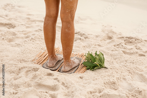 Women's feet stand on a Sadhu board with sharp nails on a white sand beach. practice yoga, meditation, concentration. close-up