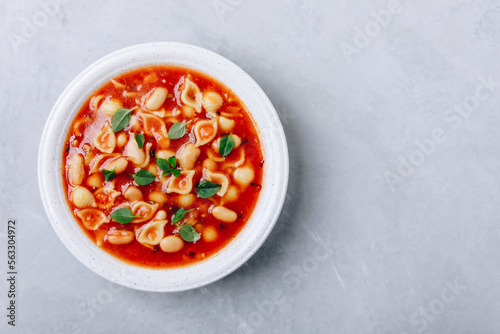 Tomato soup. Minestrone soup. Tomato bean and pasta soup bowl on gray stone background.