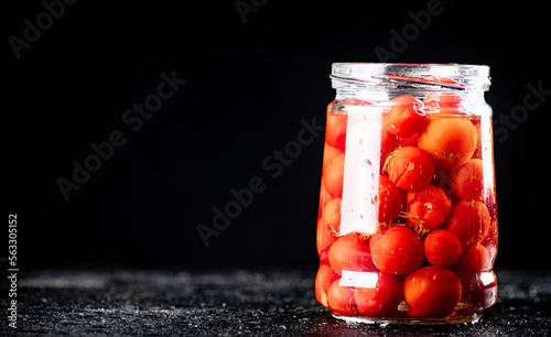Pickled tomatoes in a glass jar on the table. 