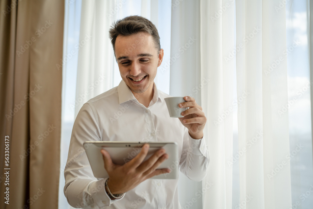 man wear white shirt hold cup of coffee and digital tablet at window man wear white shirt hold cup of coffee and digital tablet at window