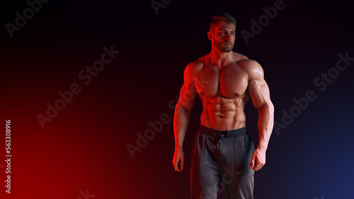 Handsome shirtless male bodybuilder with stylish haircut, wearing sports shorts, posing in a studio. Isolated on Neon Red Blue creative light background