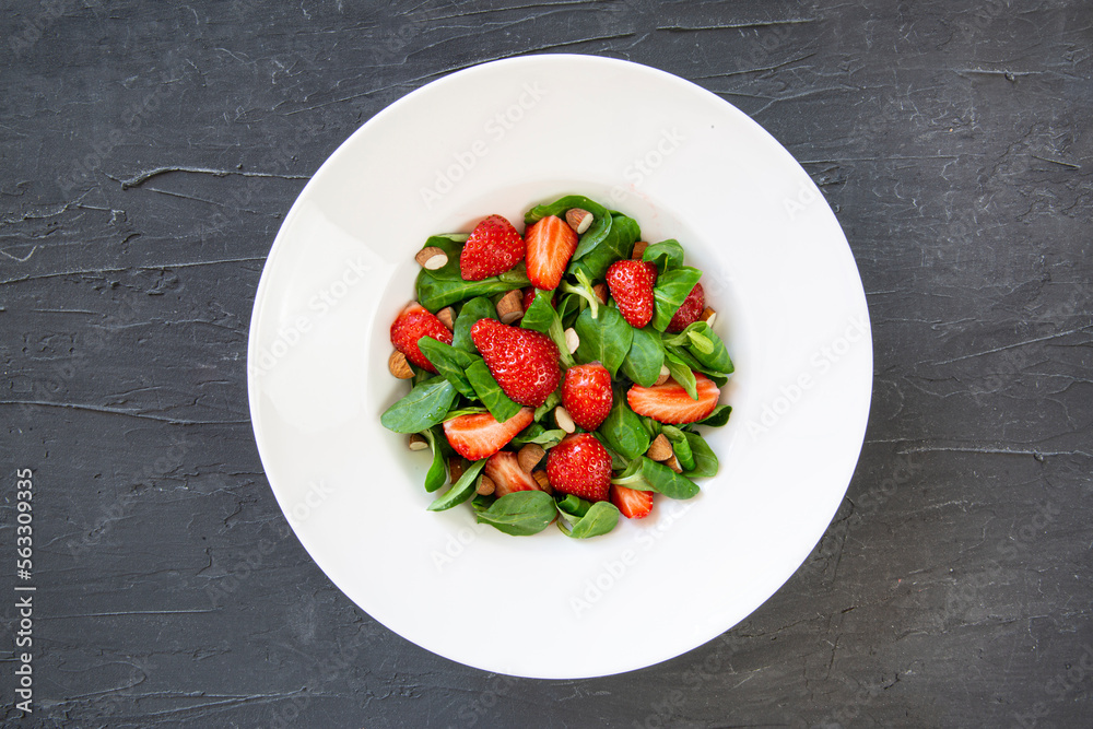 Tasty summer strawberry salad in white plate on black background, top view. Healthy diet dish. Tasty summer strawberry salad in white plate on black background, top view. Healthy diet dish.