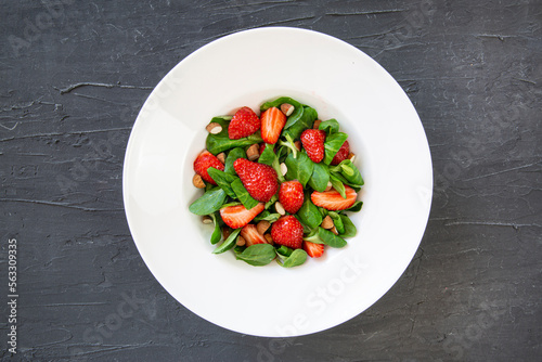 Tasty summer strawberry salad in white plate on black background, top view. Healthy diet dish. 
