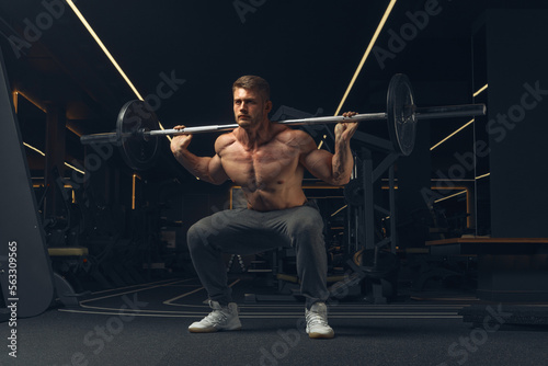 Muscular man doing squats with barbell in a gym. Male bodybuilder doing workout Confident young man doing barbell workout in gym Powerful attractive man