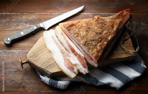Guanciale, bacon, with cutting board and knife on wooden background, close-up.