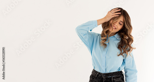 Laughing woman in blue shirt with wavy hair over white wall. Toothy smile