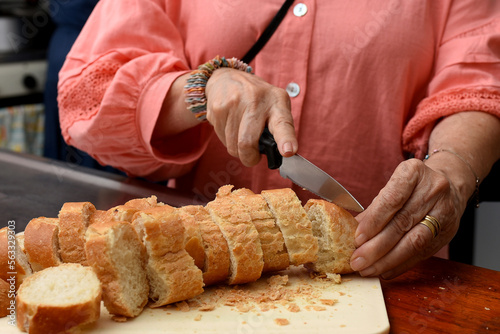 Woman cutting french bread with a knife on a wooden board. Close-up of chopped French bread on a cutting board.French bread baguette.Selective focus