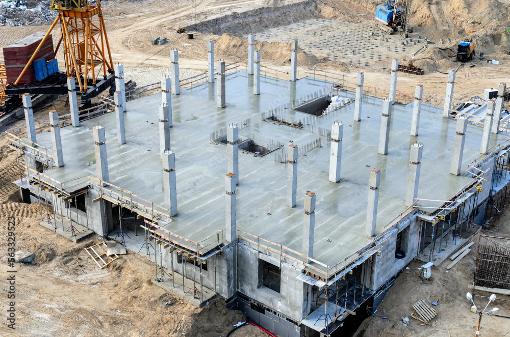 Construction site. The construction of a new house, above view on a freshly poured concrete ceiling and frame pillars, tower crane base. In the background is a pile field with drilling rig in a pit