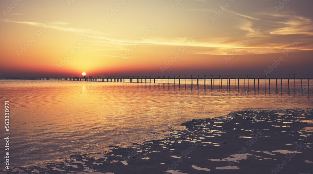Seascape with a wooden pier silhouette at sunset, color toning applied.