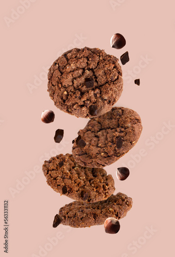 chocolate chip cookies with crushed hazelnuts flying on a beige background