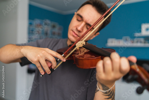 A portrait of a young guy playing or learning a violin in his home private classes online course for violin music