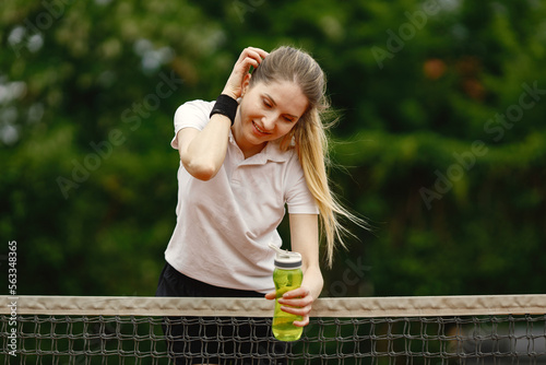 Female tennis player standing on an open tennis court and lean on a net
