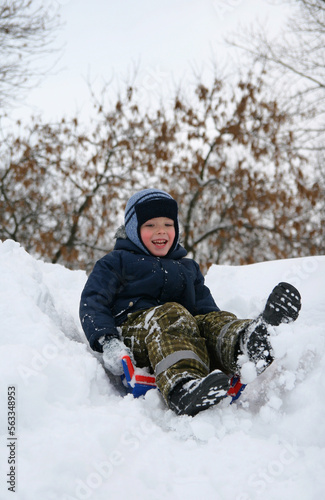A boy of 5-7 years old happily sledding in the snow.