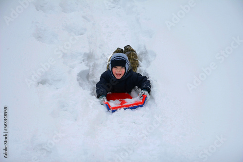 Little boy sliding on a sled in the snow outdoors in winter.