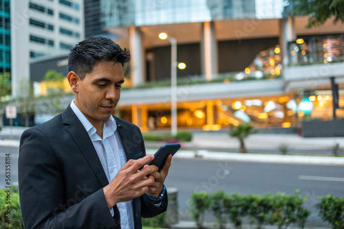 A portrait of a young smiling, happy, successful Mexican business man, executive walking outside down the street using mobile phone. 