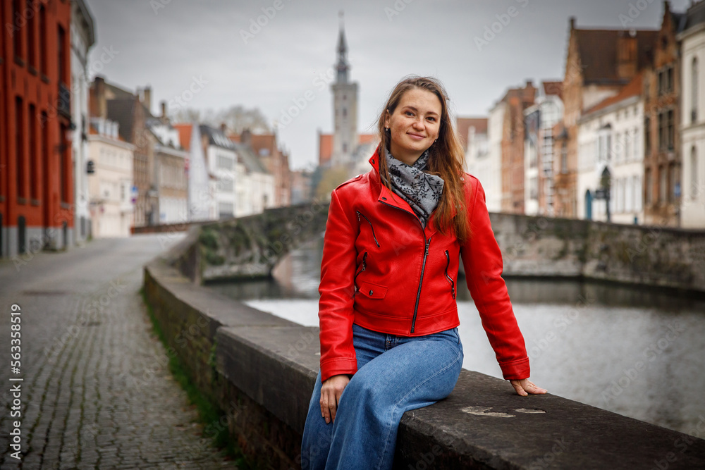 Traveling old Europe. Beautiful woman as a tourist in Brugge, Belgium in the red jacket in autumn.
