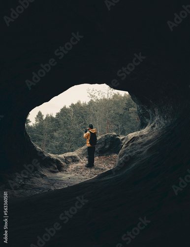 person standing in an end open cave, taking pictures
