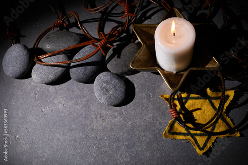 Holocaust memory day. Barbed wire, stones, yellow star and burning candle on black background photo