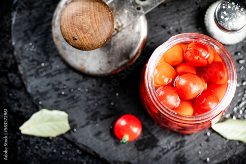 On a stone board are pickled tomatoes in a jar. 