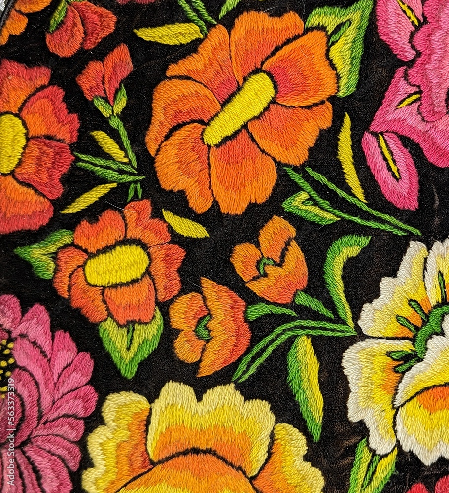 Mexican traditional embroidery in yellow, pink, orange and green on black background. Flowers and leaves