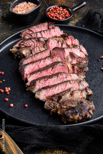 Juicy medium beef Rib Eye steak slices, on plate, on old dark rustic background