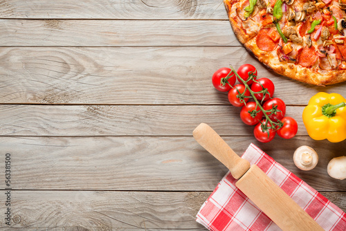 Pizza, tomatoes, mushrooms, bell pepper and rolling pin on wooden table background. Top view with copy space.