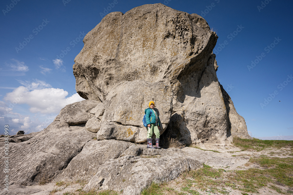 Exploring nature. Boy wear backpack hiking near big stone in hill. Pidkamin, Ukraine.