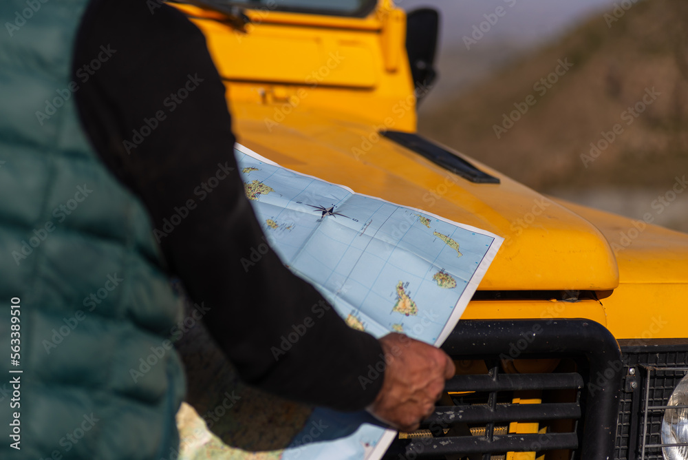 senior man in green vest, looking at a map on top of yellow 4x4 car, outside image, horizontal image, copy space,concept of adventure, experiences.