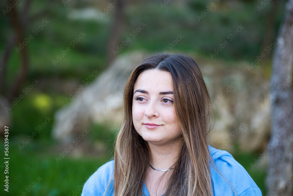 portrait of beautiful woman with blue t-shirt and green background, long brown hair, exterior image, horizontal with copy space. portrait of beautiful woman with blue t-shirt and green background, long brown hair, exterior image, horizontal with copy space.