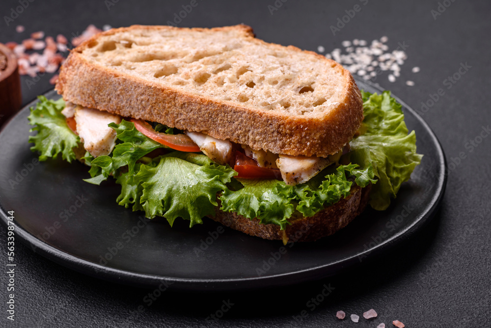 Fresh tasty sandwich with chicken, tomatoes and lettuce on a black plate Fresh tasty sandwich with chicken, tomatoes and lettuce on a black plate