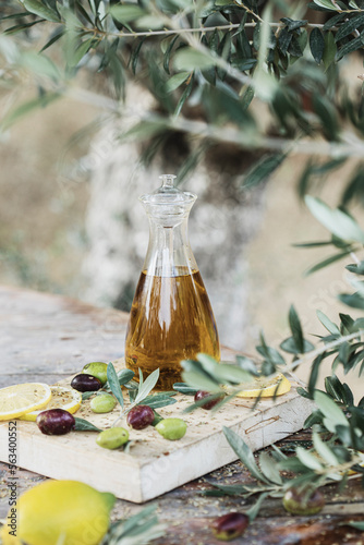 Olive oil bottle and olive oil in glass on old wooden table under olive tree.