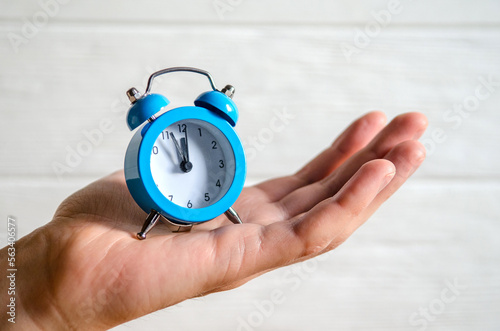 Fototapeta Naklejka Na Ścianę i Meble -  Classic arrow blue alarm clock on a man hand on white background, concept of the passage of time