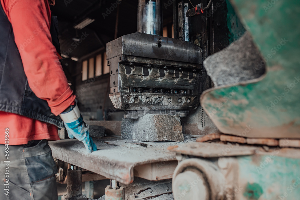 A worker in heavy industry breaks stone blocks using large machines. Granite and stone processing industry. A worker in heavy industry breaks stone blocks using large machines. Granite and stone processing industry.