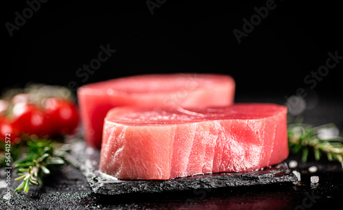 Raw tuna on a stone board with rosemary and tomatoes.