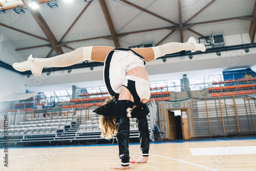 Full shot of a cheerleader in handstand doing a split in a sports hall. The stands are in the background. High quality photo