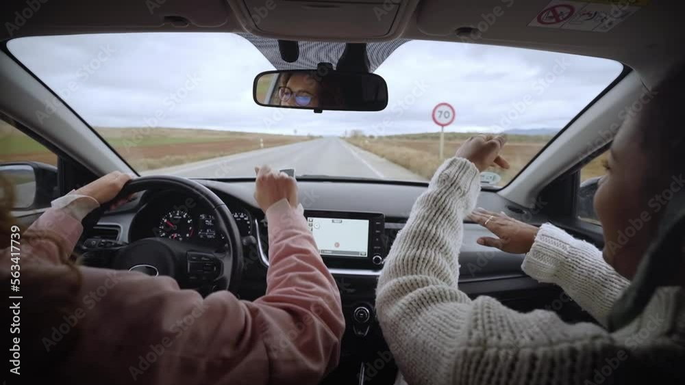 Funny women singing happy while driving automobile. Cool two young girls dancing lively music in car while driving in the countryside. Friends having fun concept. Rear view. Slow motion.