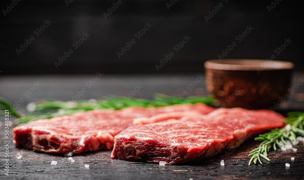 Raw steak with rosemary and spices on the table. 