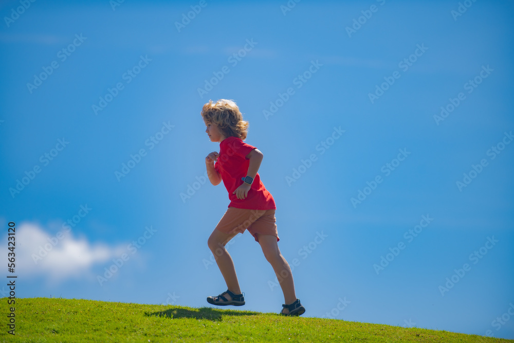 Sporty kid boy running on green grass and blue sky. Sporty kid running in nature. Active healthy child boy runner run outdoor. Sporty kid boy running on green grass and blue sky. Sporty kid running in nature. Active healthy child boy runner run outdoor.
