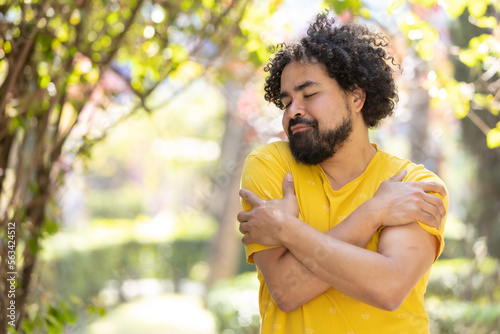 young Mexican man with beard and afro hugging himself, self love concept