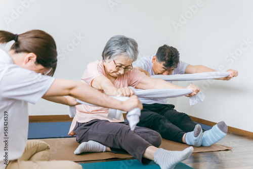 老人ホームでタオル体操・運動・リハビリするシニア・高齢者の男女と理学療法士・介護士・トレーナー 