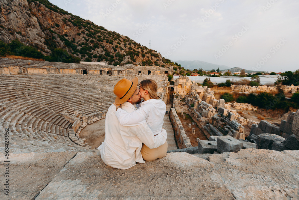 Fototapeta premium Happy lover couple tourist archaeologist in hat background old tomb Myra Ancient City in Demre to Antalya, archaeology of Turkey