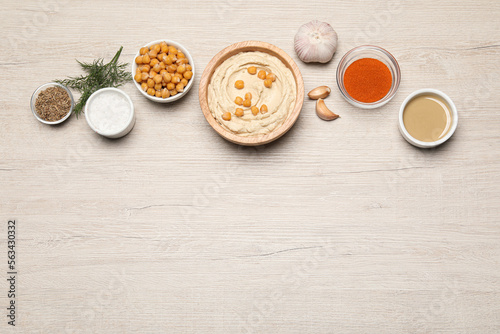 Bowl with delicious hummus and different ingredients on white wooden table, flat lay. Space for text