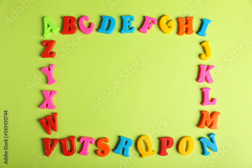 Frame made of many colorful magnetic letters on light green background, flat lay with space for text